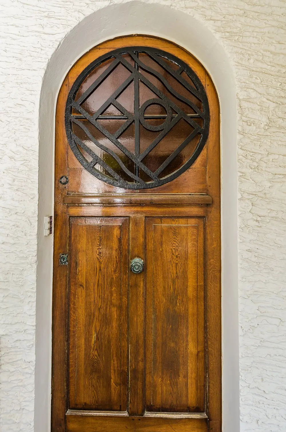 Porte d'entrée en chêne cintrée avec oculus en ferronnerie géométrique, villa Les Opales